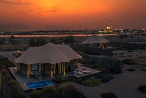 A desert resort with two tents, a pool, and a view of a city skyline at sunset.