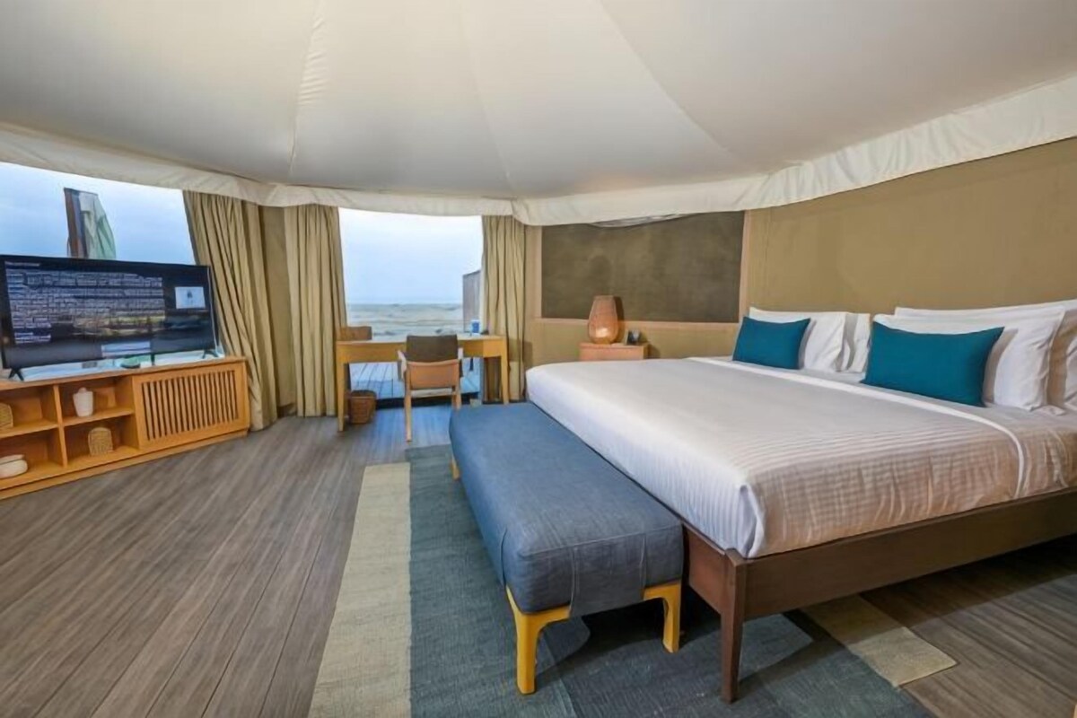 A hotel room with a bed, a desk, a television, and a view of the sea.