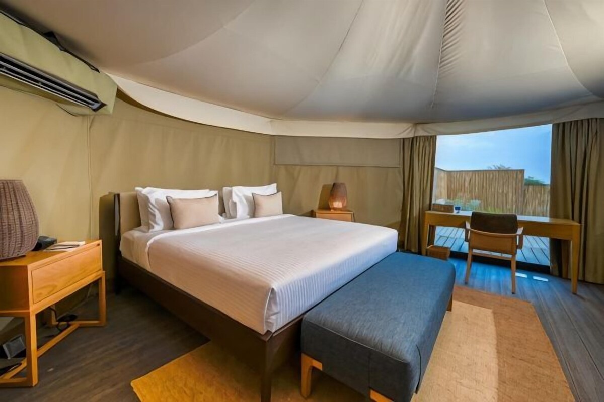 A tent-style room with a bed, bedside table, lamp, and a view of the outdoors.