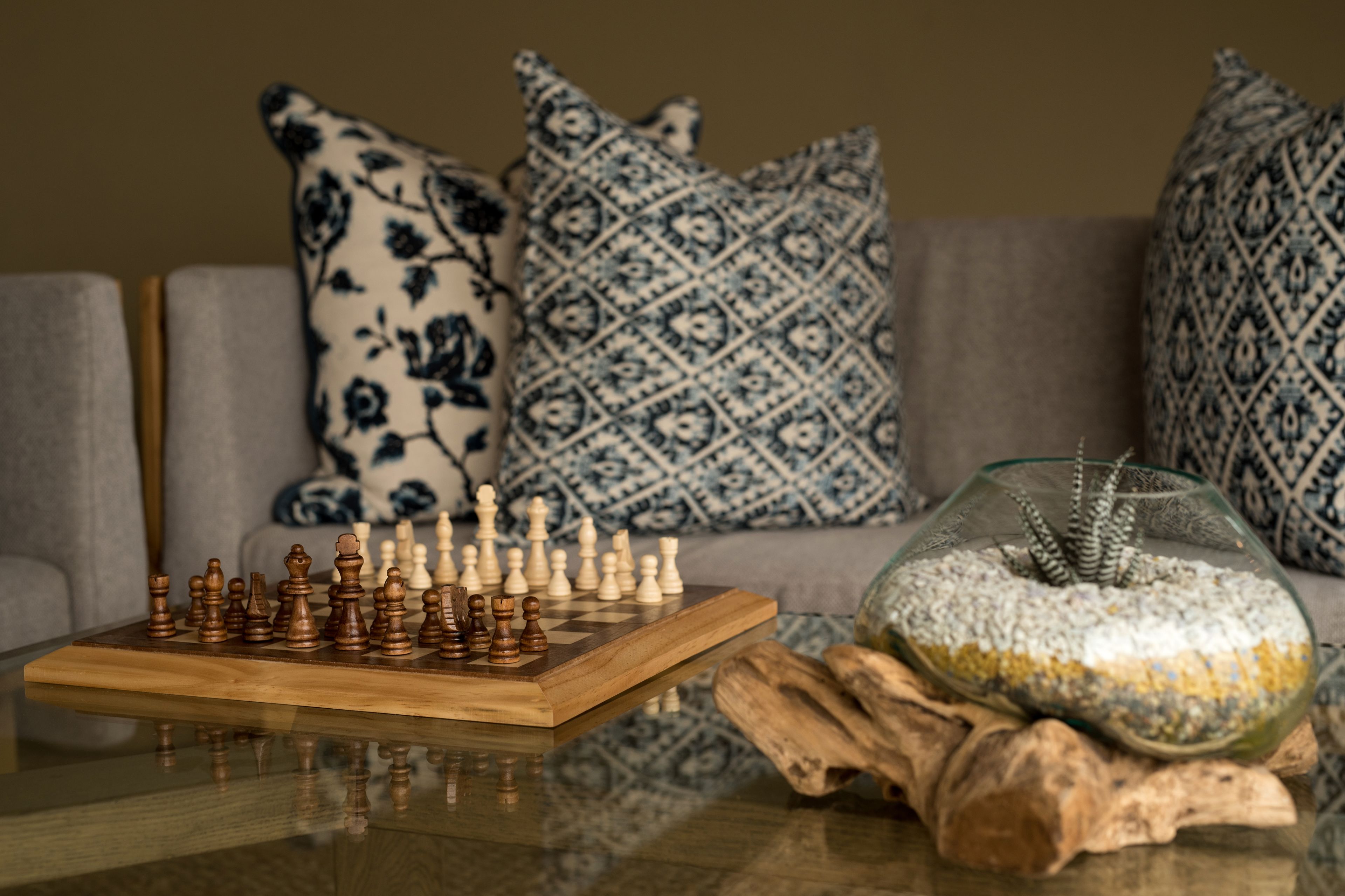 A chessboard on a glass table with a decorative bowl and a wooden log.