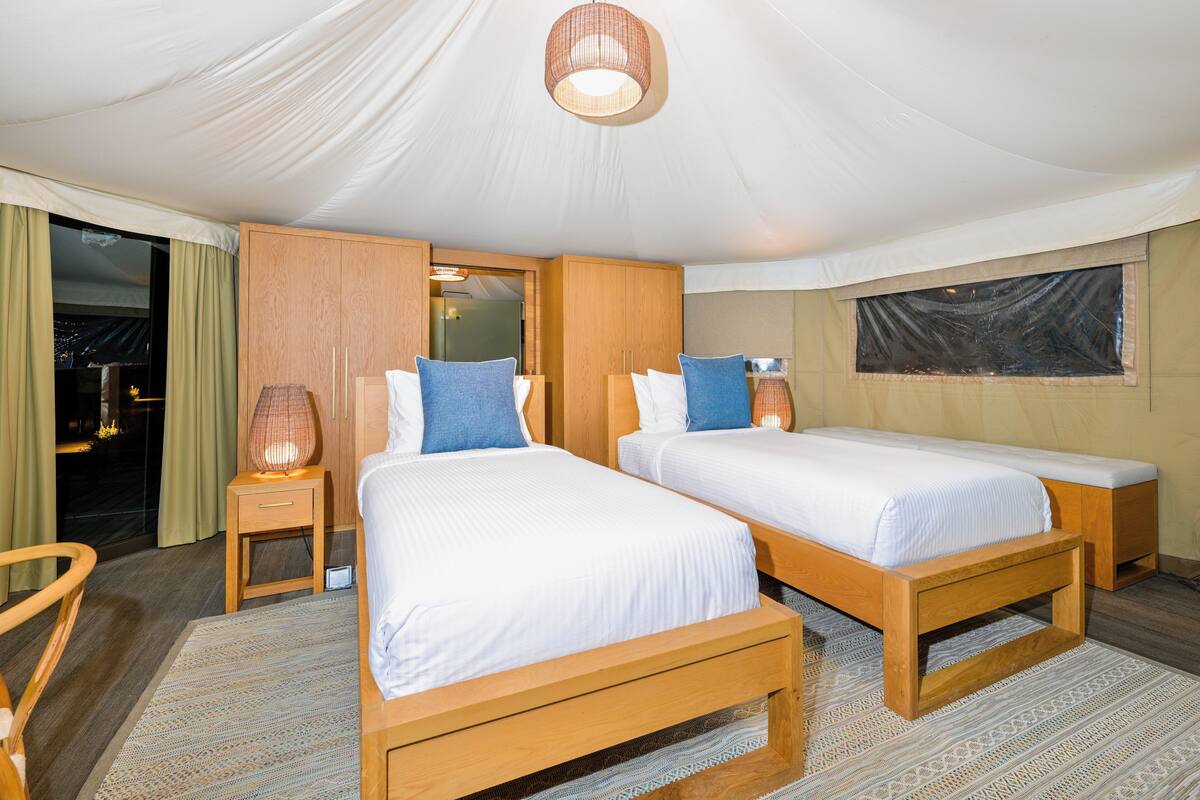 A tented accommodation room with two beds, wooden furniture, and a view of the city at night.