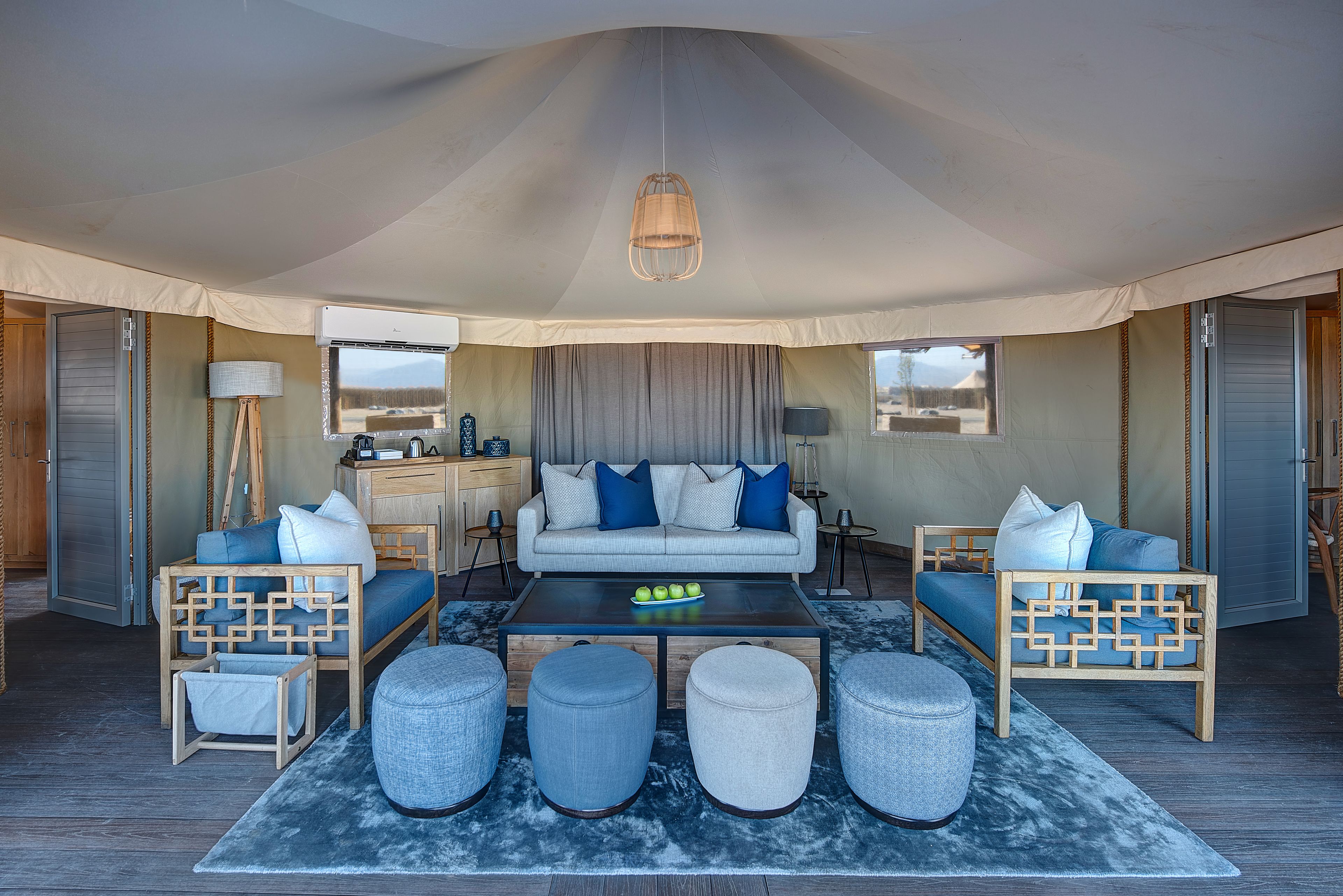 Un espace de vie aménagé sous une tente, comprenant un canapé, des poufs et une table basse.