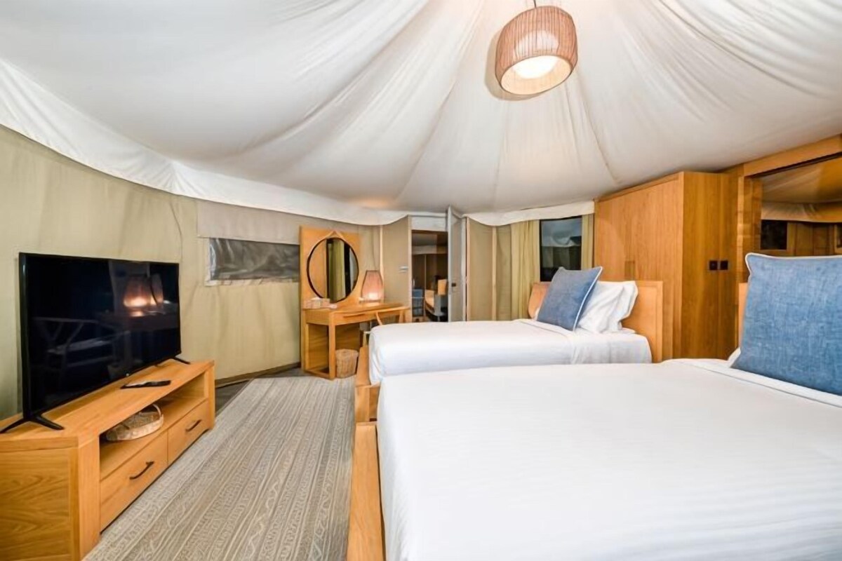 A tent-style room with two beds, a TV, a mirror, and a wooden cabinet.