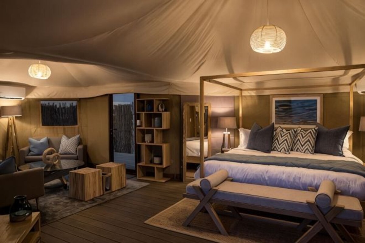A tented room with a bed, a sofa, a reading chair, and a small table.