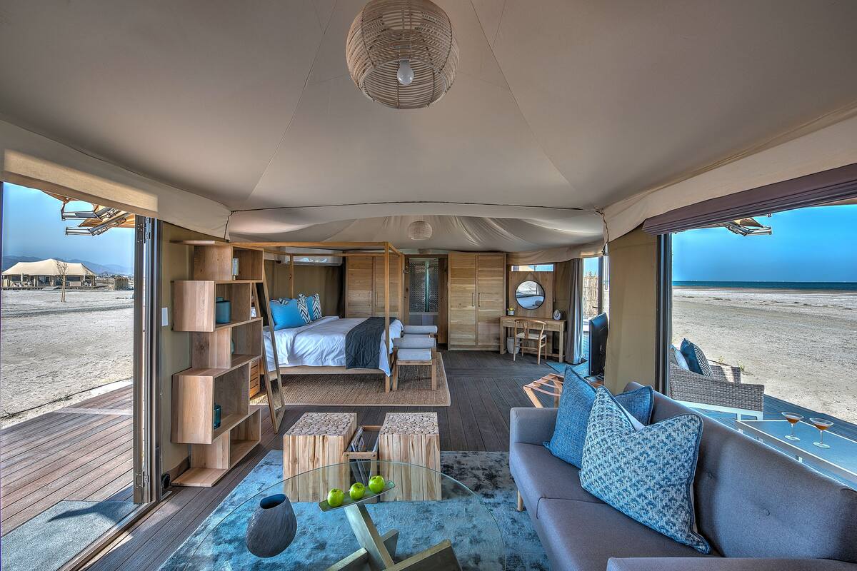 A spacious room with a bed, seating area, and a view of the beach.