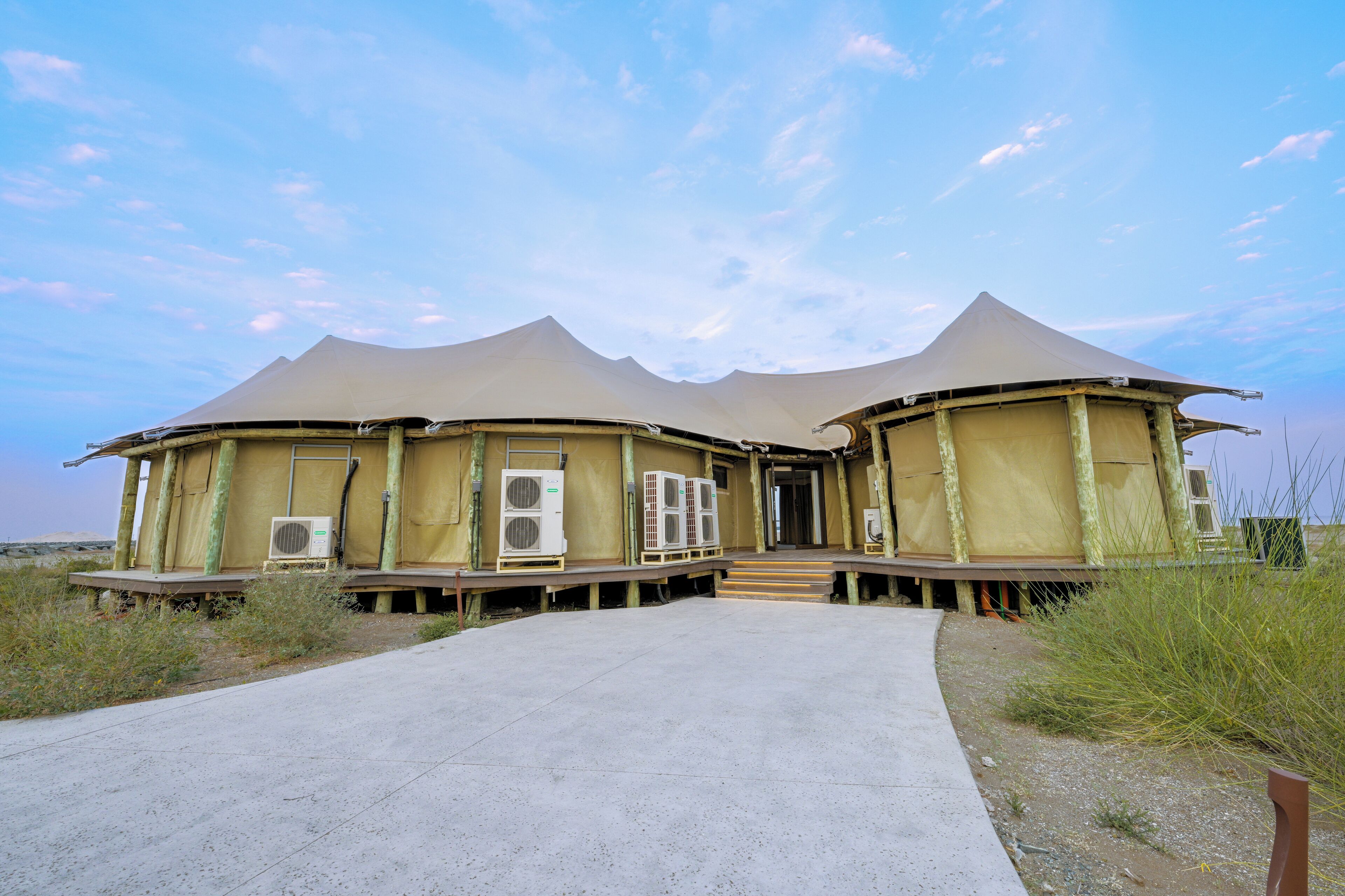 Edificio de estilo yurt con dos pisos y un camino de hormigón que lleva a la entrada.