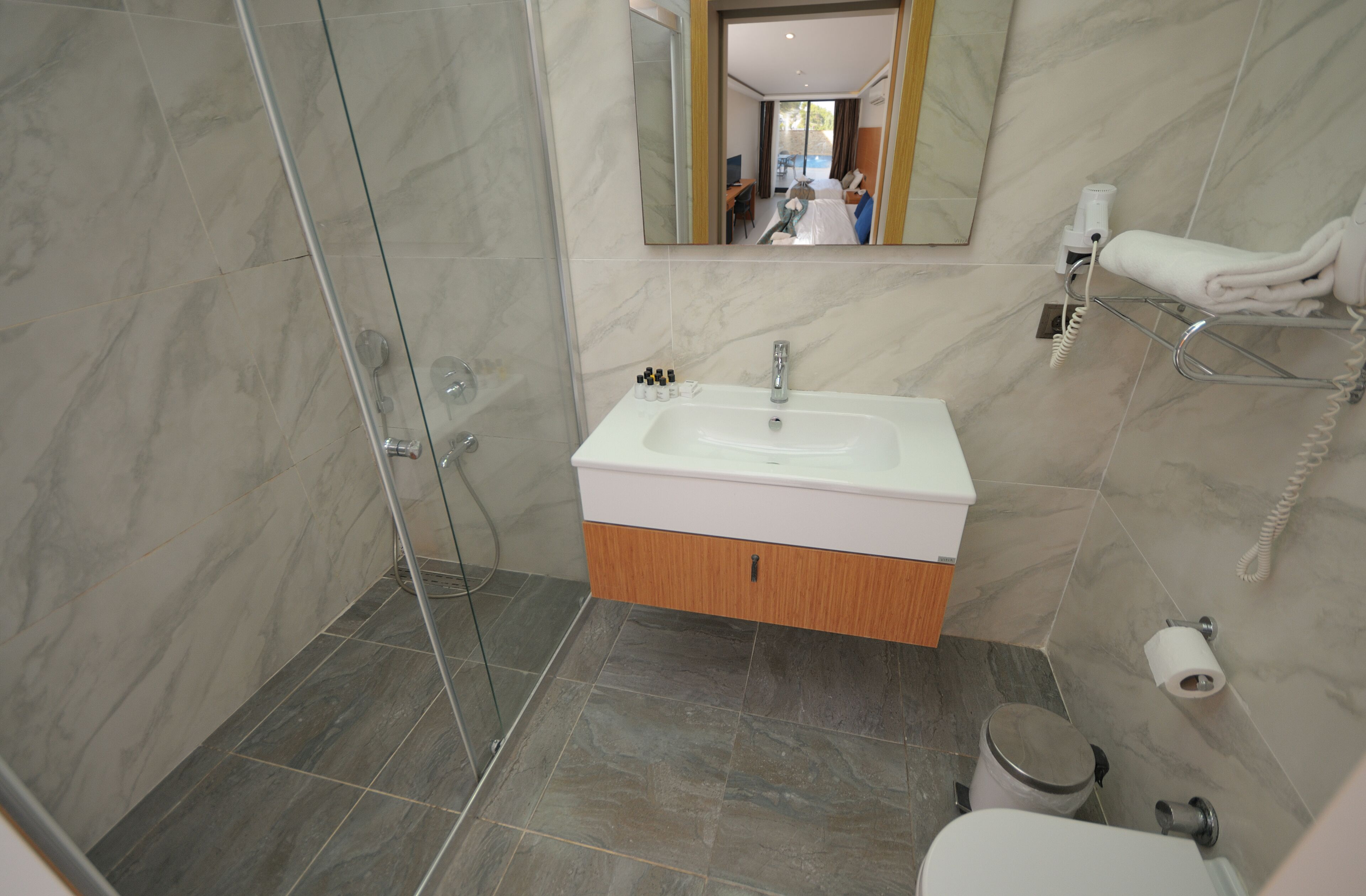 A modern bathroom with a glass shower enclosure, a white sink with a wooden cabinet, and a toilet.