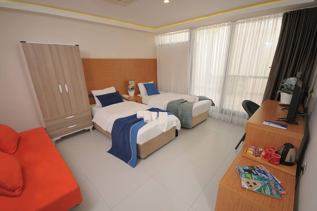 Habitación de hotel con dos camas, un escritorio, una silla, un armario y una ventana con cortinas.