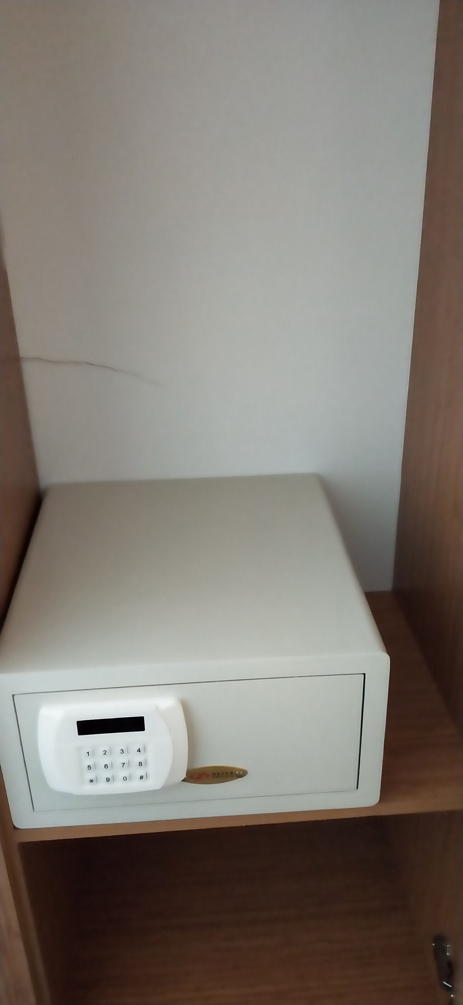 A white electronic device with a keypad and a small screen, placed on a wooden shelf.