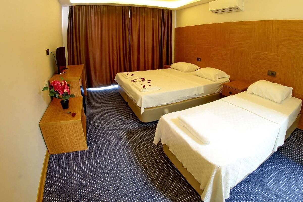 Habitación de hotel con dos camas, un escritorio de madera, una mesita con un florero y un amplio ventanal con cortinas.