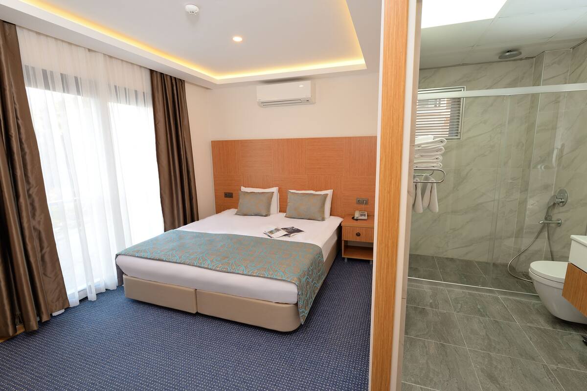 Una habitación de hotel con una cama grande, una mesita de noche y una zona de ducha.