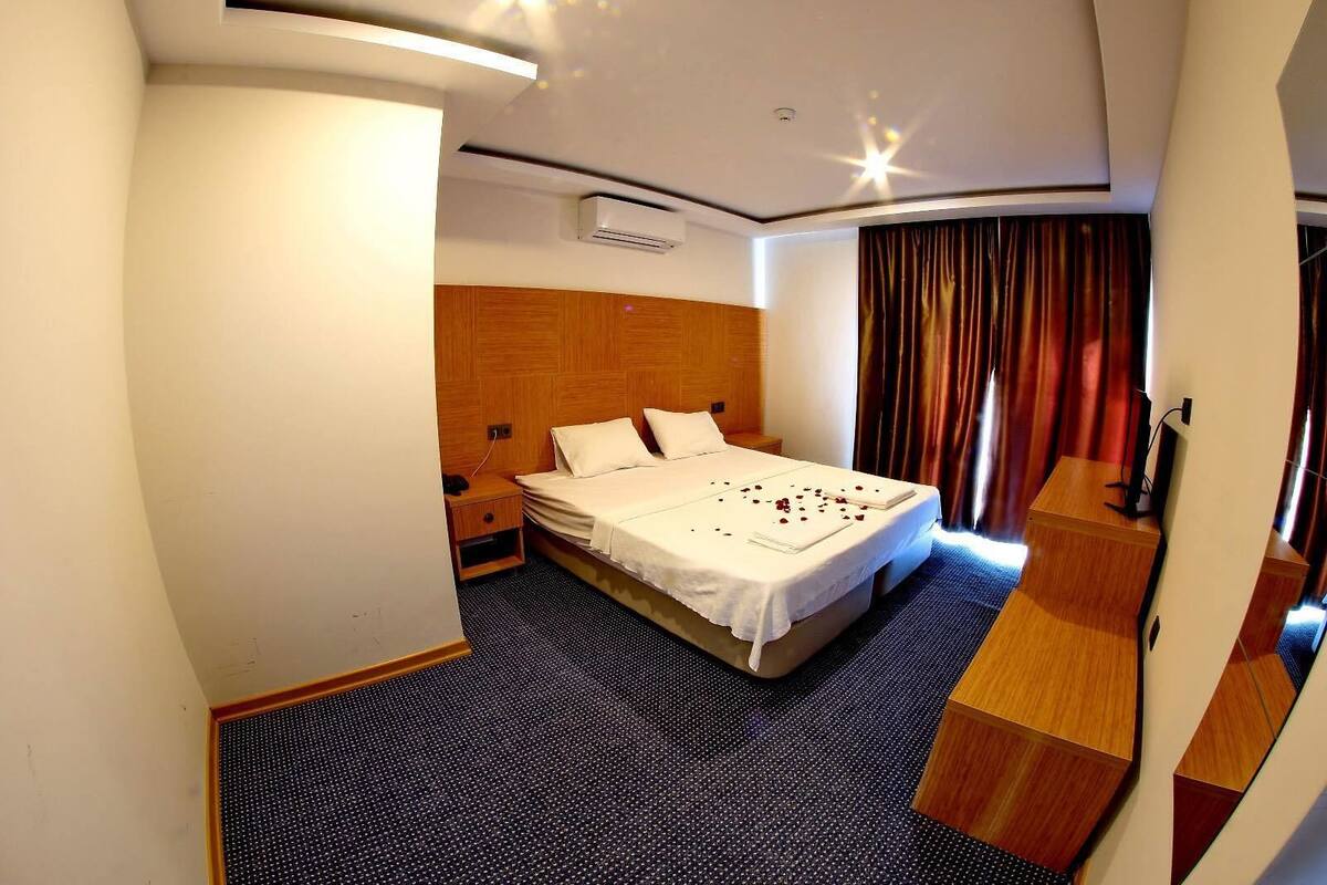 Una habitación de hotel con cama, escritorio, televisión y ventana con cortinas.