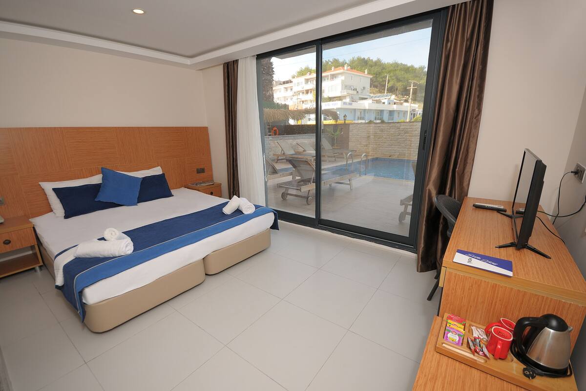 Habitación de hotel con cama, escritorio, computadora y vista a la piscina y edificios cercanos.