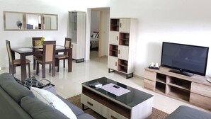 A modern living room with a sofa, coffee table, TV, and a dining area with chairs and a table. - Appartement Dayer (Abidjan)