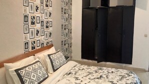 A bedroom with a bed, patterned pillows, a wall with framed pictures, and a black wardrobe. - Appartement Dayer (Abidjan)