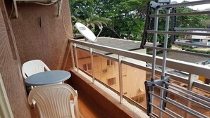 A balcony with a small table and two chairs, a satellite dish, and a view of buildings and trees. - Appartement Dayer (Abidjan)