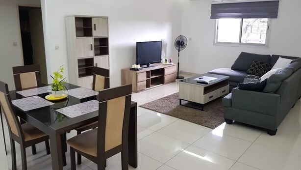 A modern living room with a dining area, a sofa, a TV, and a fan. - Appartement Dayer (Abidjan)