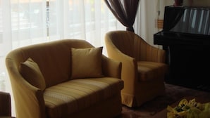 A living room with a sofa, a piano, and a window with sheer curtains.