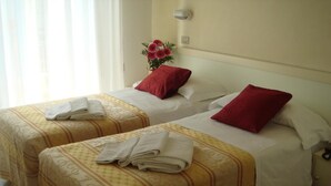 A hotel room with two beds, each with a red pillow, white linens, and a floral arrangement on the nightstand.