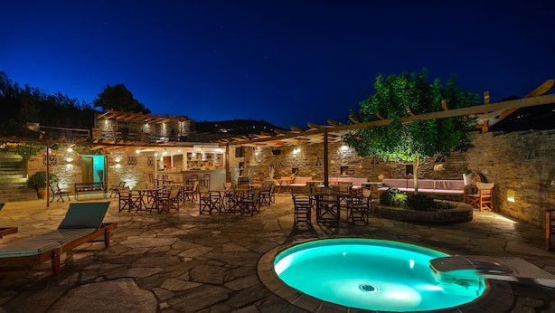 A stone patio with a swimming pool, outdoor seating, and a stone building with a bar area. - Villa Sofia (Andros)