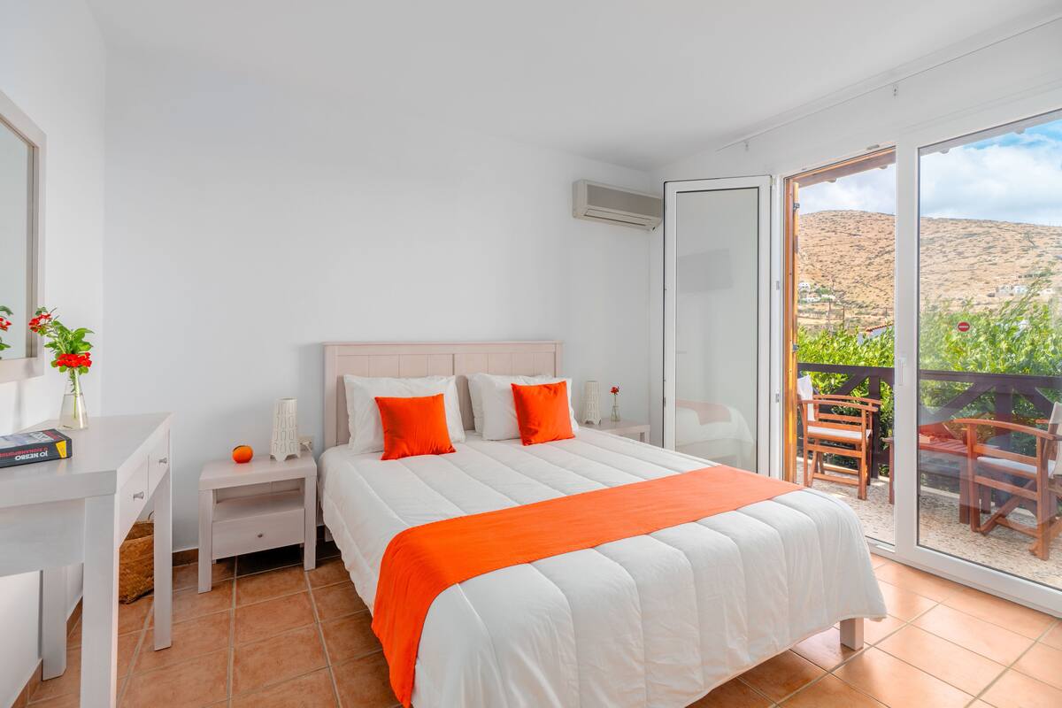 A bedroom with a bed, nightstands, a desk, and a balcony with a view of the landscape.