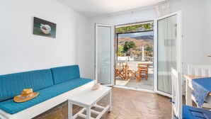 A room with a blue sofa, a white table, and a glass door leading to an outdoor area with a table and chairs. - Villa Sofia (Andros)