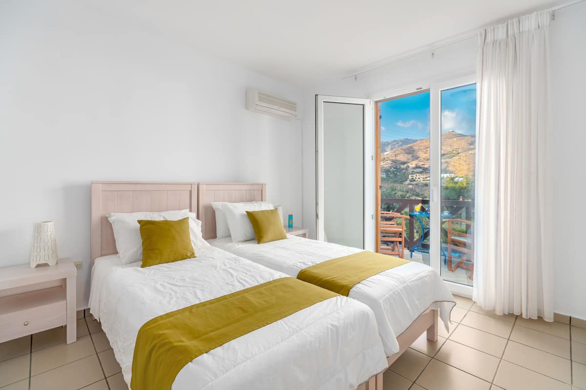 A hotel room with two beds, a nightstand, and a sliding glass door leading to an outdoor area.