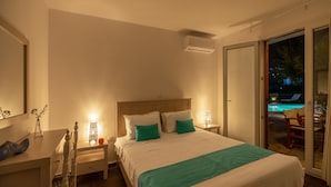 A bedroom with a bed, bedside tables, a nightstand, a lamp, and a view of a swimming pool through a sliding glass door. - Villa Sofia (Andros)