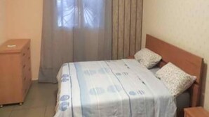 A bedroom with a bed, a wooden nightstand, a dresser, and a window with curtains.