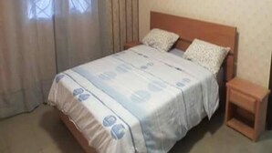 A bedroom with a bed, curtains, a nightstand, and a window.