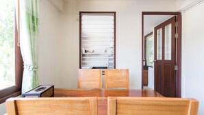 A dining area with a wooden table and chairs, a glass cabinet with shelves, and a door leading to another room. - Lemon House (Rawai)