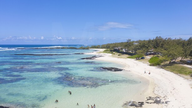A beach with clear turquoise water, a sandy shore, and a line of trees and buildings along the coastline. - Villa Banian (Trou d'Eau Douce)