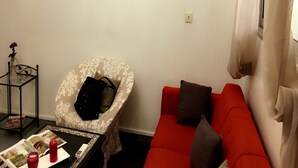 A living room with a red sofa, a patterned armchair, a small table with magazines, and a wall-mounted air conditioner. - Résidence Bimbois (Abidjan)