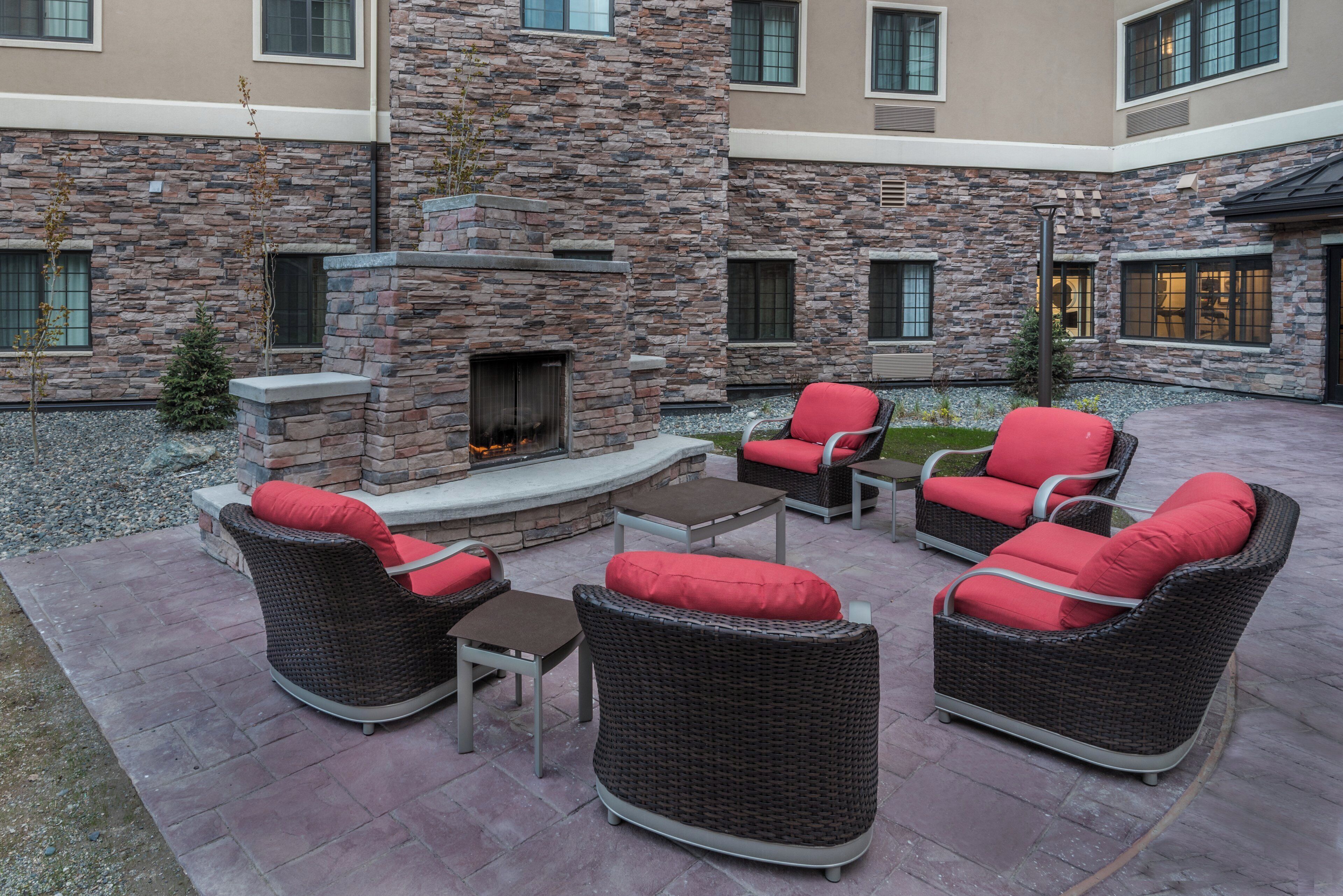 Un patio al aire libre con mobiliario de mimbre, una chimenea de piedra y vistas del exterior del edificio.