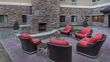 Un patio al aire libre con mobiliario de mimbre, una chimenea de piedra y vistas del exterior del edificio.