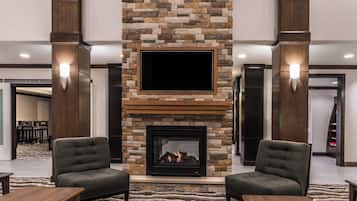 A hotel lobby with a stone fireplace, two armchairs, a flat-screen TV, and a patterned rug.