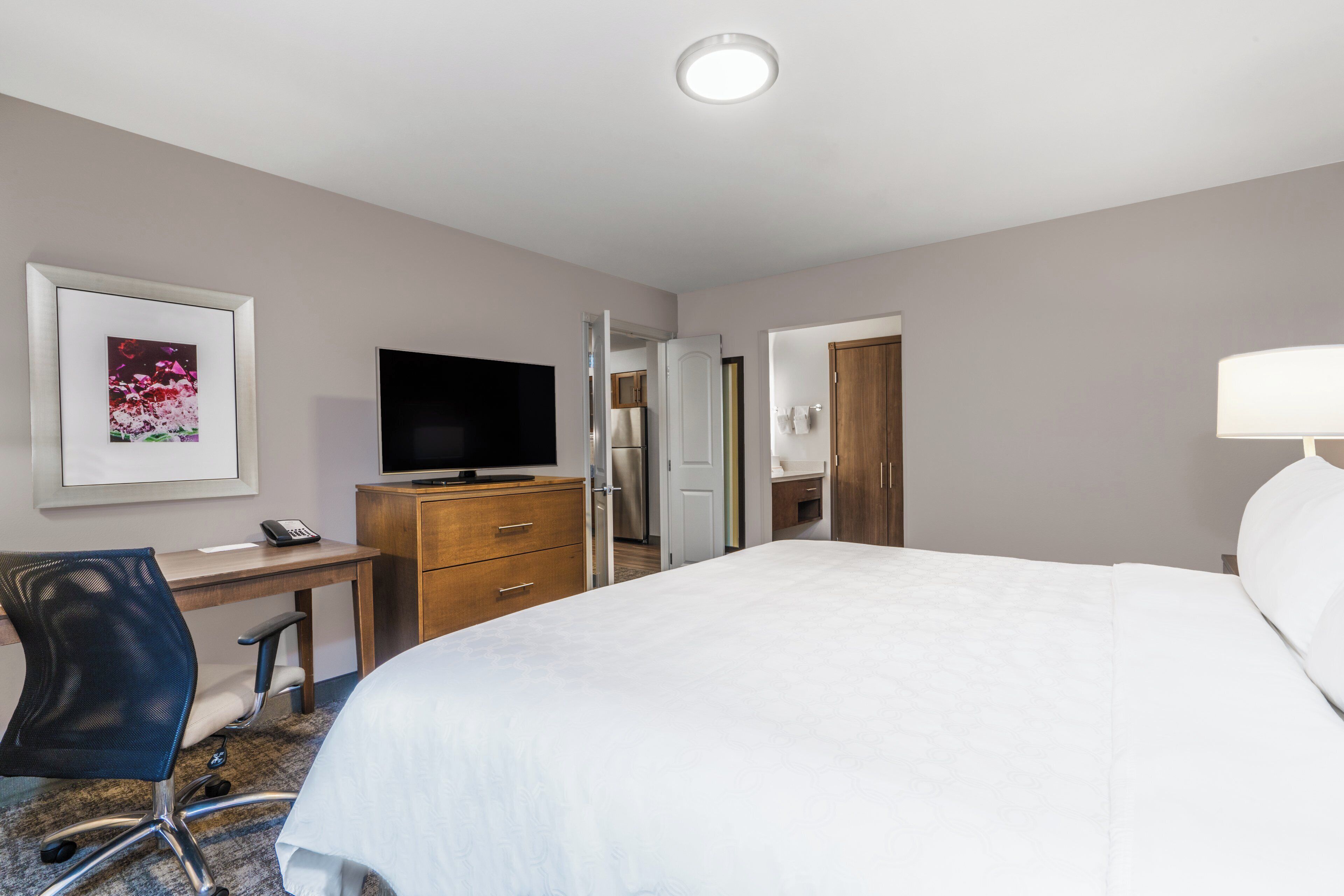 A hotel room with a bed, desk, chair, television, and a door leading to a bathroom.