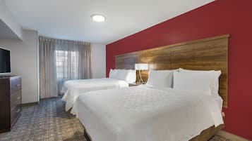 Habitación de hotel con dos camas, televisión, escritorio y ventana con cortinas.
