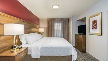 Quarto de hotel com cama, abajures, televisão, cômoda e um quadro na parede.