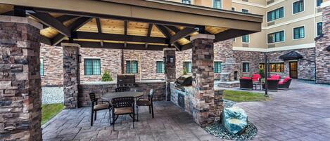 A covered patio area with stone pillars, a barbecue grill, and outdoor seating.