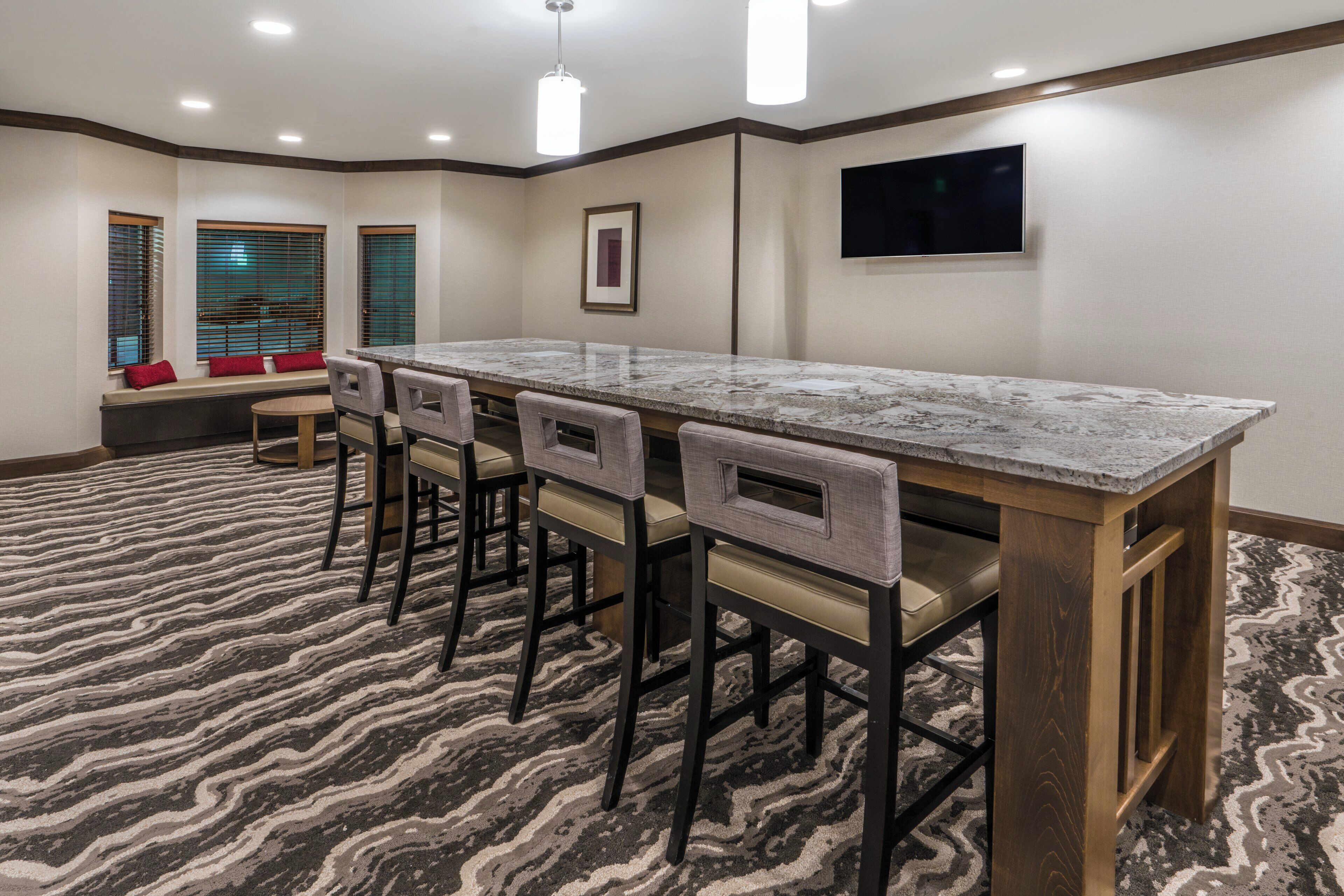 A hotel room with a marble bar, four barstools, a television mounted on the wall, and a patterned carpet.
