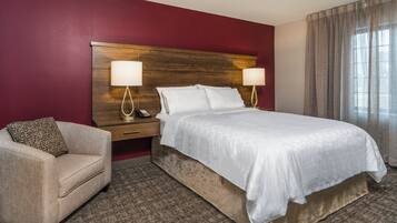 Habitació d'hotel amb un llit gran, dues làmpades de nit, una taula de nit, una cadira i una paret vermella decorativa.