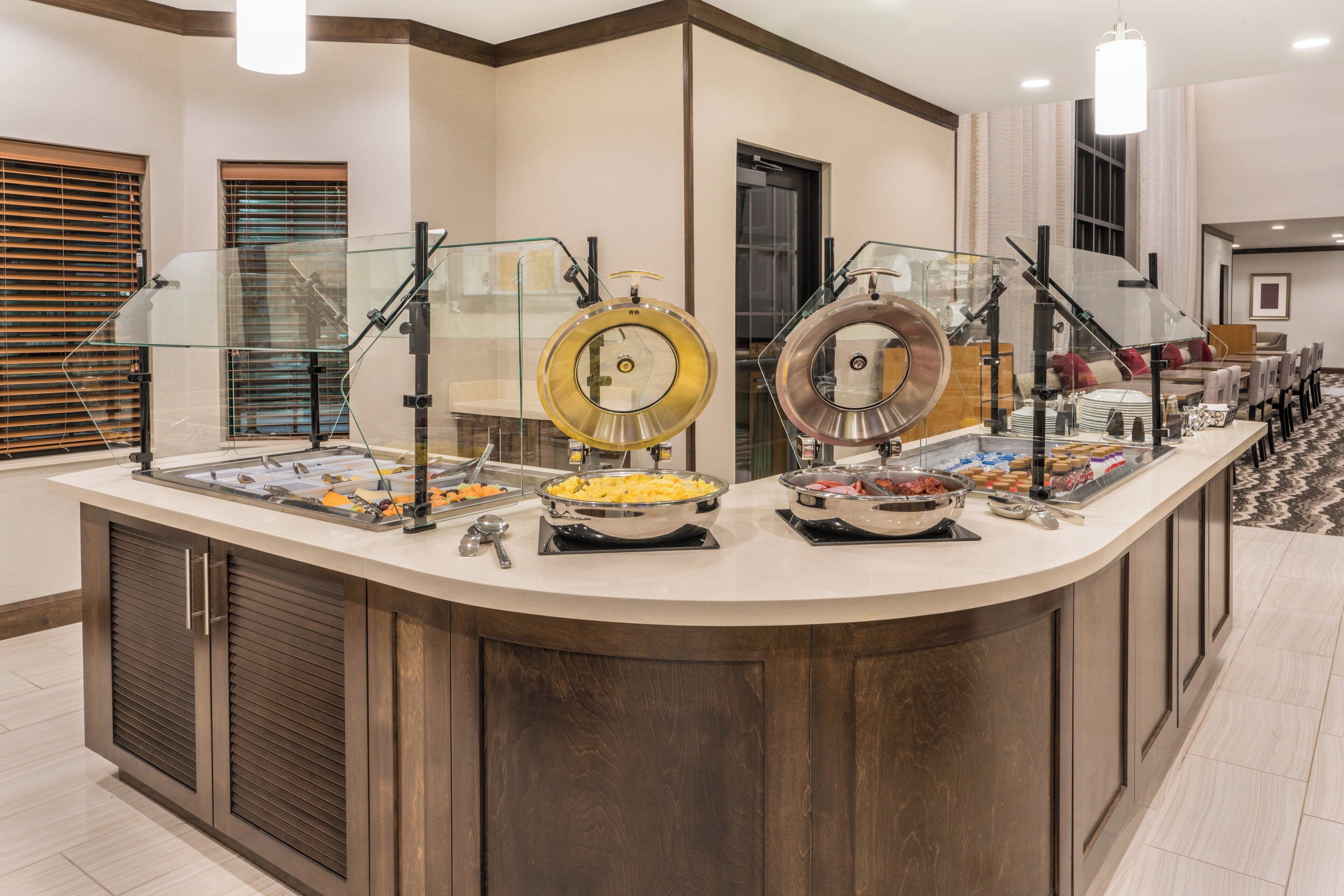 Un buffet avec plusieurs présentoirs de nourriture, un espace repas avec des tables et des chaises, et un aménagement intérieur moderne.