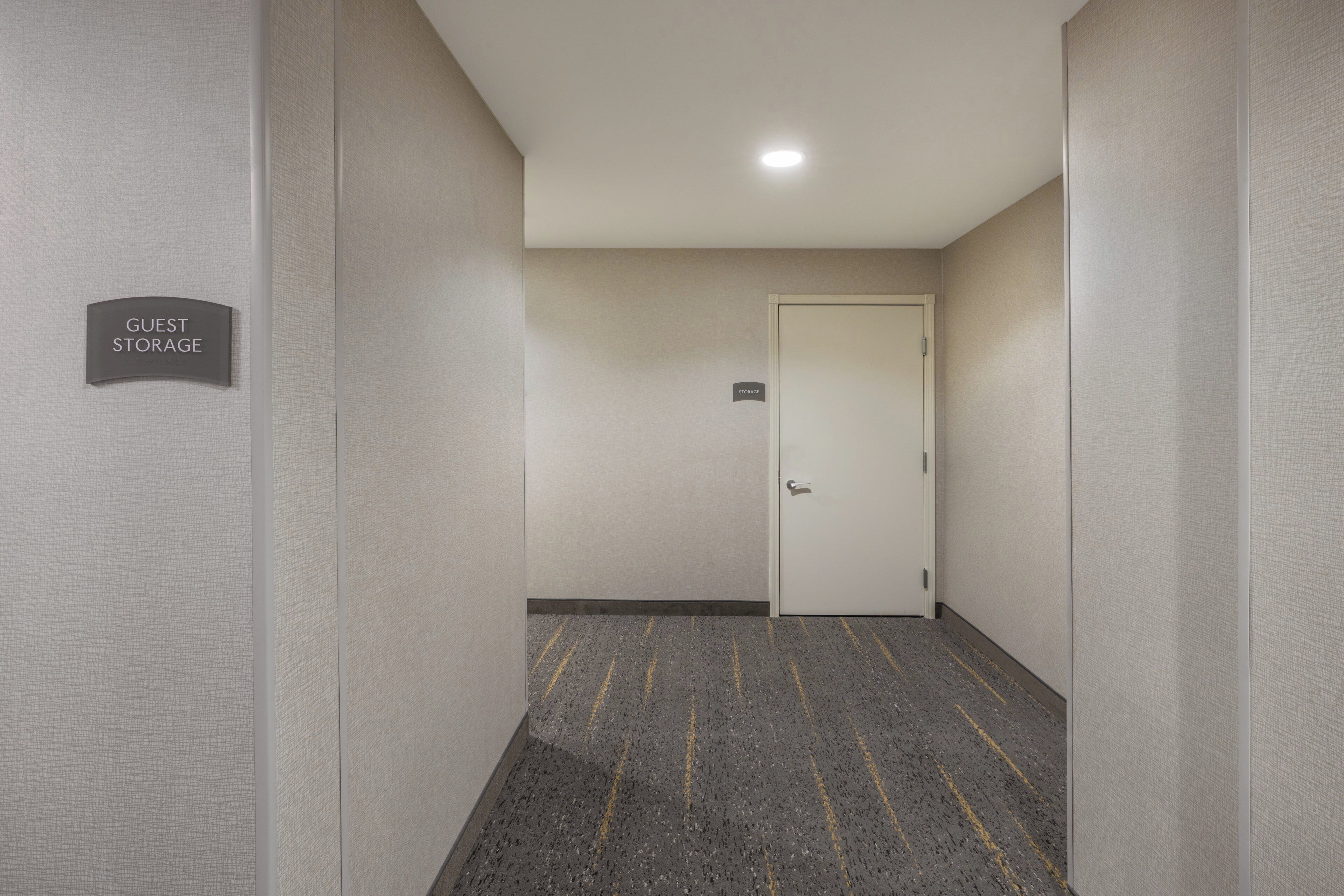 Un couloir avec une pancarte indiquant «Espace de rangement pour les invités», une porte marquée «Rangement» et une moquette à motifs avec des rayures jaunes.