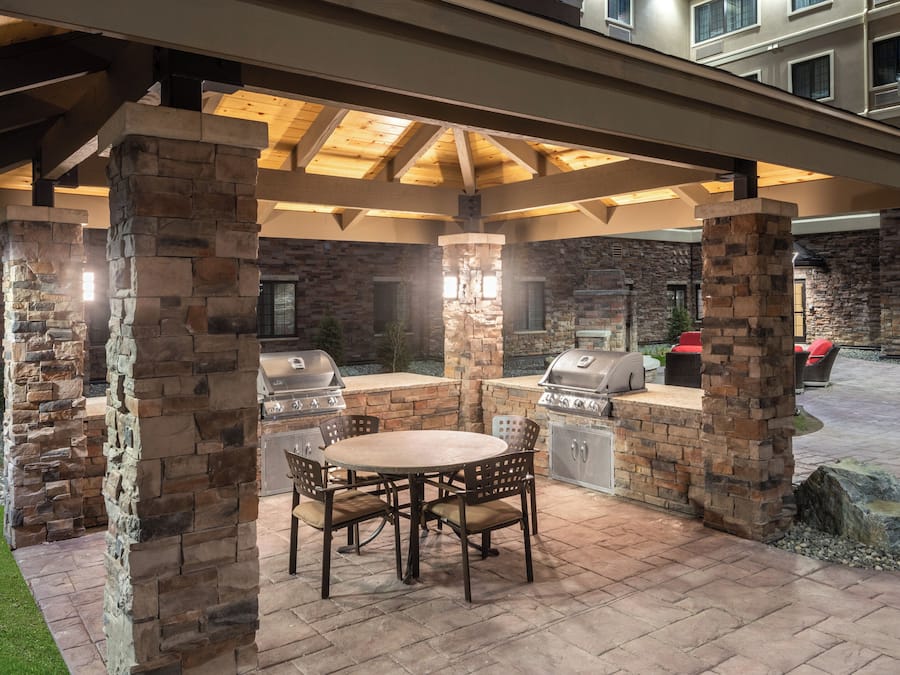 An outdoor patio with stone pillars, a round table, and two barbecue grills.