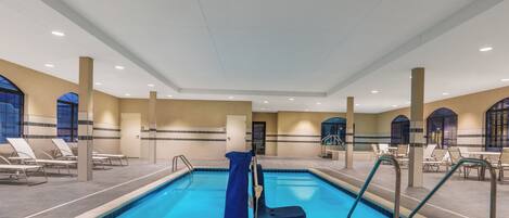 An indoor swimming pool with clear blue water, surrounded by lounge chairs and a seating area with tables.