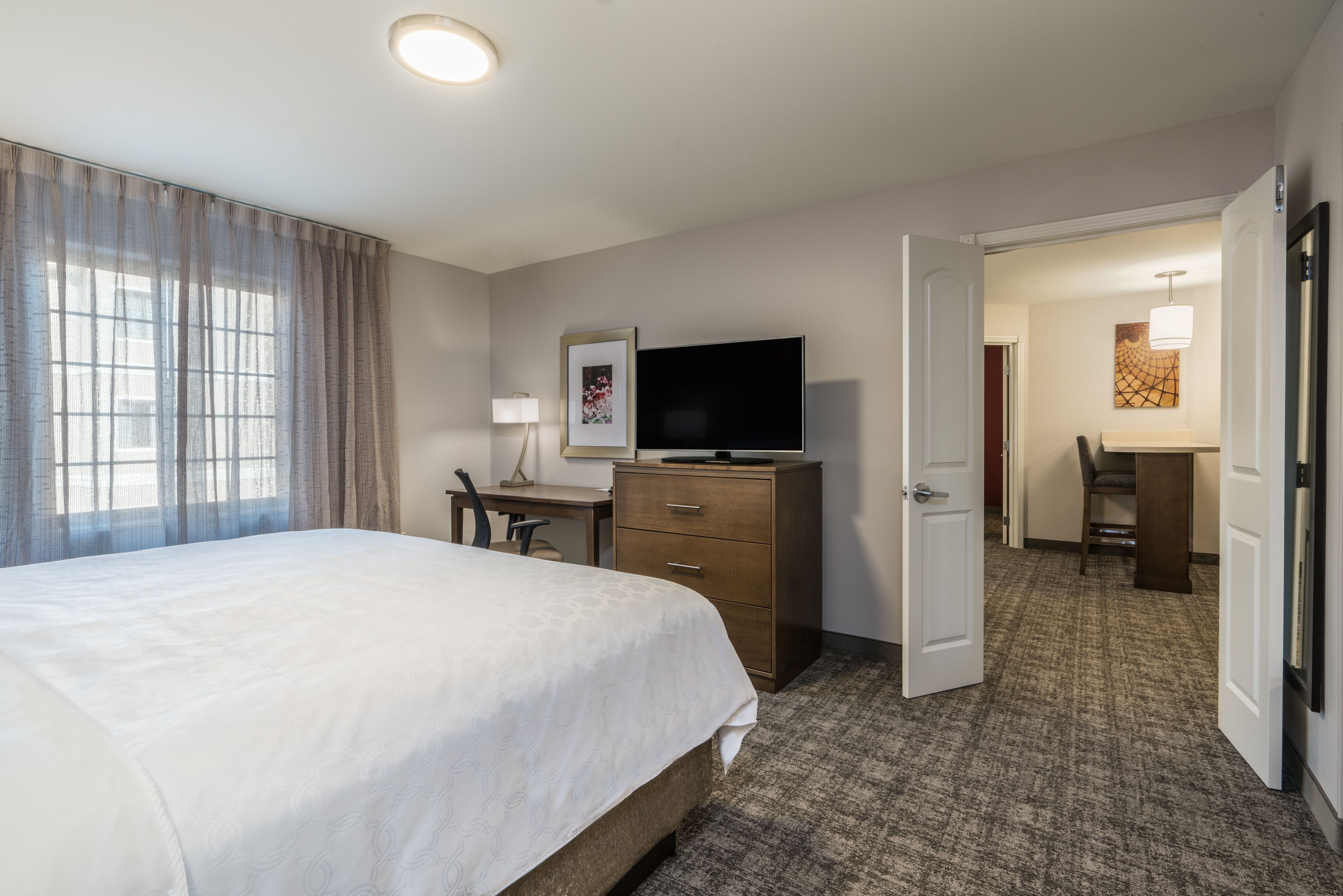 Una habitación de hotel con cama, escritorio, televisión y puerta que da a otra habitación.