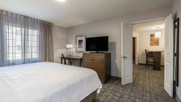 Una habitación de hotel con cama, escritorio, televisión y puerta que da a otra habitación.