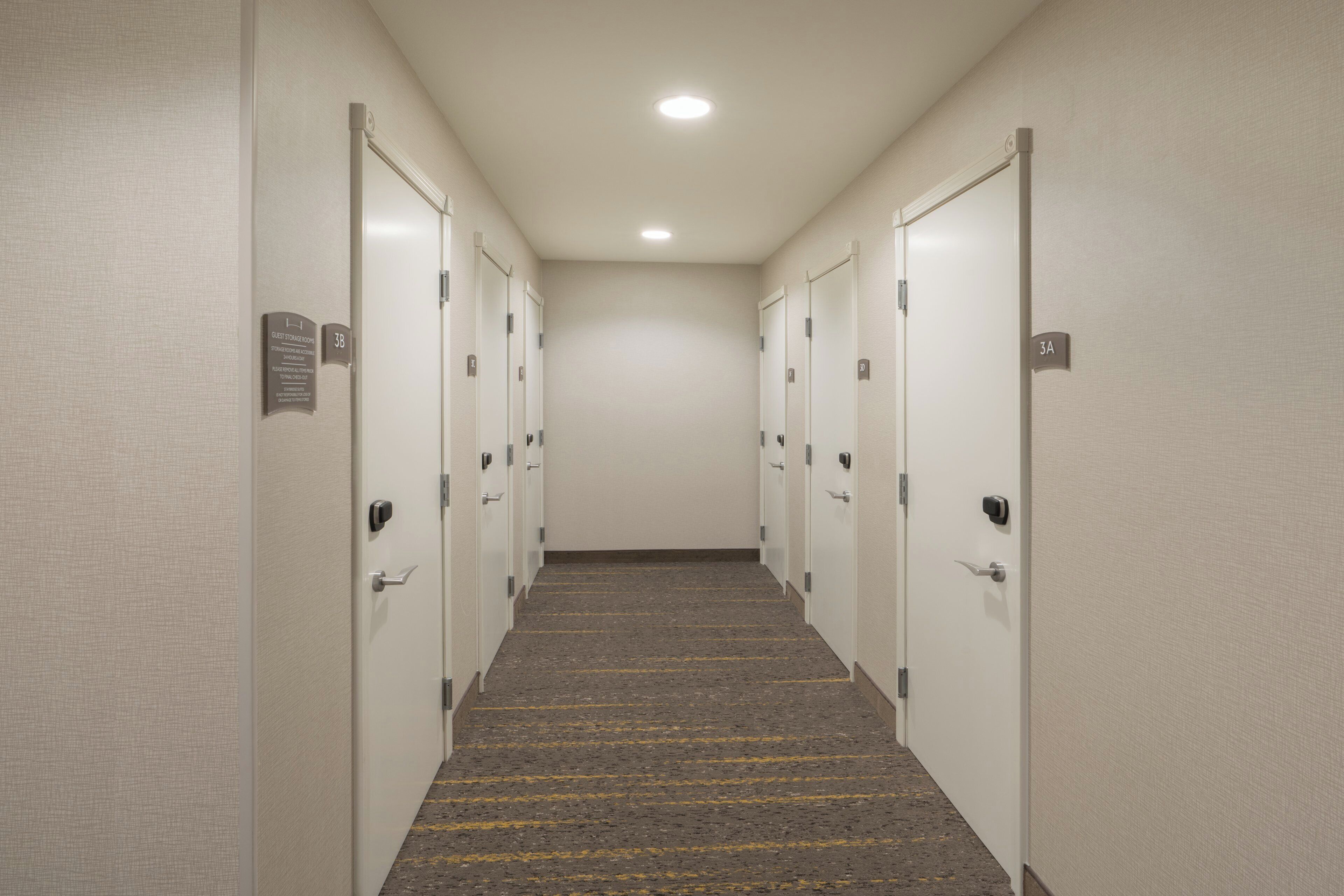 Pasillo de hotel con puertas identificadas como 3A, 3B y 3C, que dan a cuartos de almacenamiento para huéspedes.