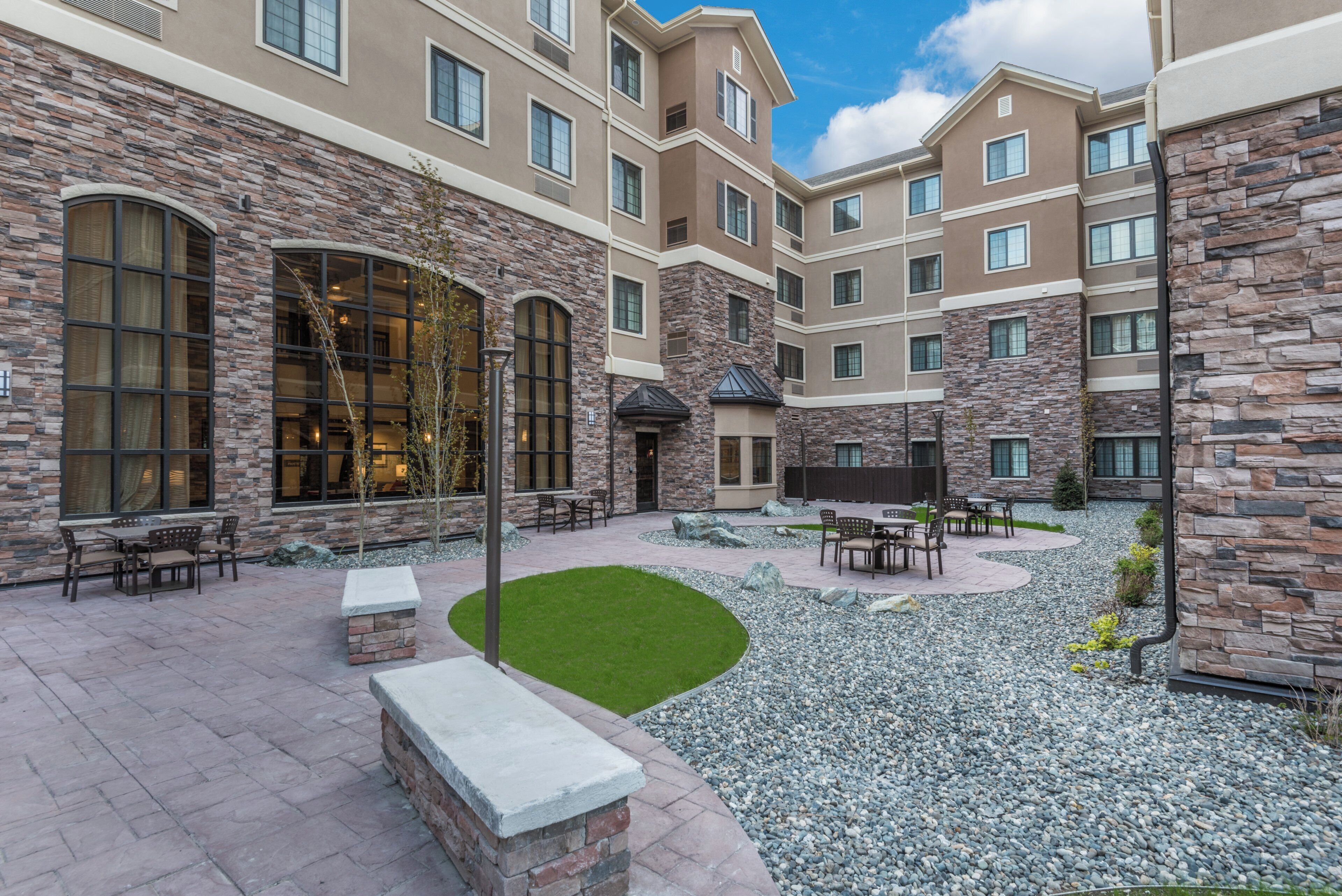 A courtyard with outdoor seating, a stone wall, and a building with multiple windows.